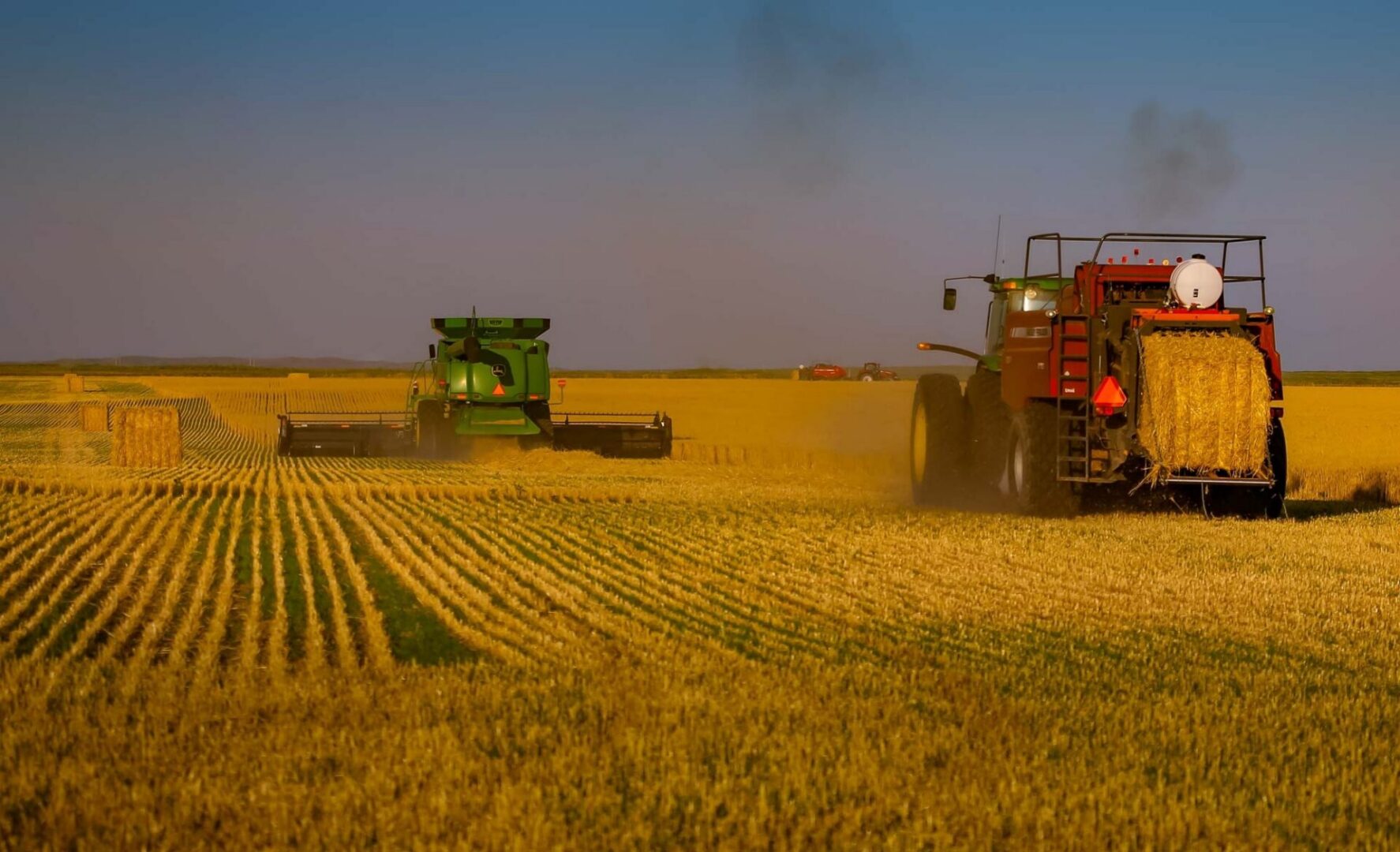 Combine harvester working in a wheat field, with a tractor in the foreground and a sky in the background